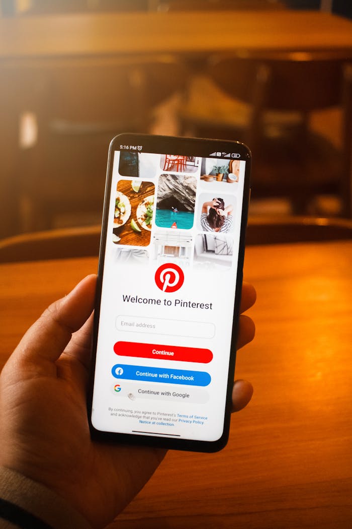 Close-up of a hand holding a smartphone displaying the Pinterest login screen indoors.